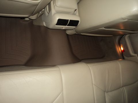 2004 Mercury Grand Marquis - The rear interior of a vehicle shows beige leather seats and custom-fit WeatherTech floor mats in the footwell.