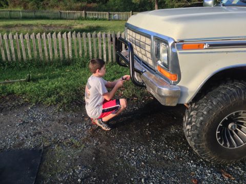 1979 Ford Bronco - A young boy works on the front of a truck, which appears to be from the late 1970s or early 1980s.