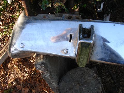 1973 Ford Ranchero - A detached chrome bumper section, showing signs of wear and rust, is supported by wooden logs outdoors.