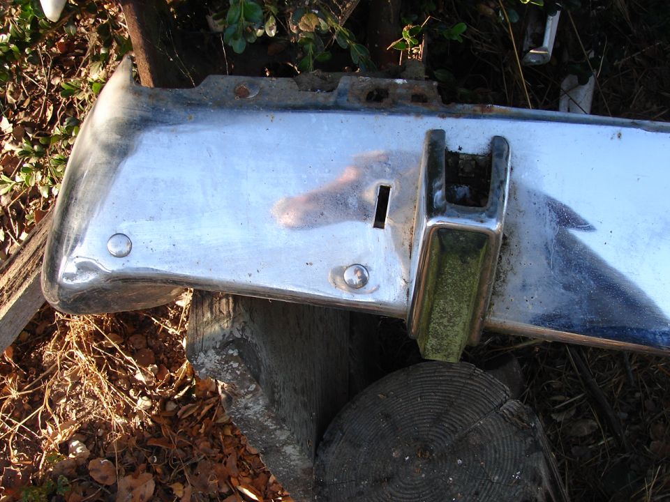 Chrome bumper section with a rectangular slot and a U-shaped bracket, resting on logs