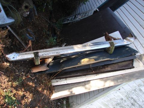 1973 Ford Ranchero - A collection of automotive parts, including a chrome bumper, are stored outdoors.