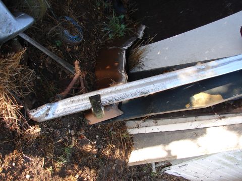1973 Ford Ranchero - Fragment of a chrome bumper and a dark panel lie amongst dirt and grass.