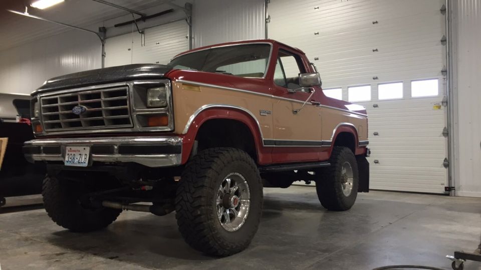 Red and tan Ford Bronco with lifted suspension and large tires parked in a garage