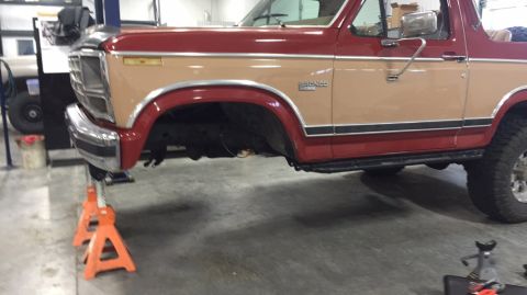 1984 Ford Bronco - This two-tone red and tan 1984 Ford Bronco is shown on jack stands, likely for maintenance or repair.
