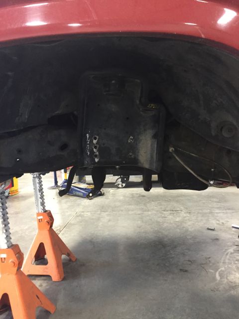 1984 Ford Bronco - The undercarriage of a red vehicle is visible, supported by jack stands, with suspension parts in view.
