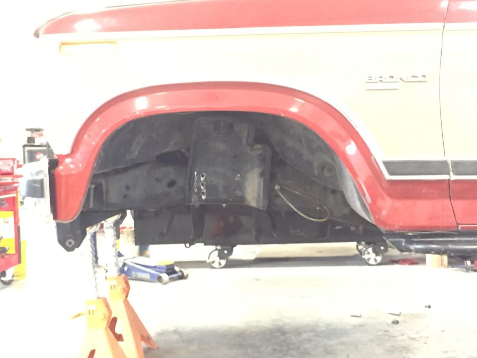 1984 Ford Bronco front wheel well and chassis on jack stands. Bronco script visible on fender