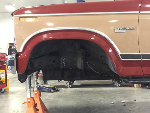 1984 Ford Bronco - The front fender and door of a two-tone Ford Bronco are visible as the vehicle is raised on jack stands.