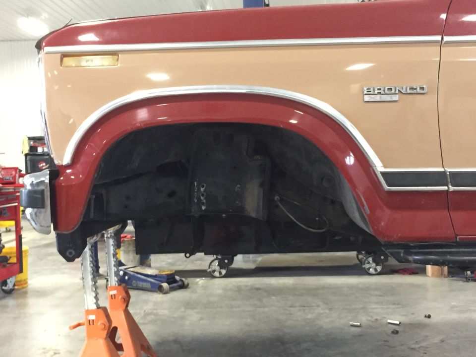 Ford Bronco with front wheel well removed, supported by jack stands