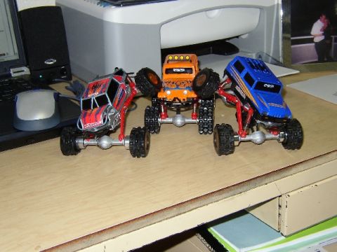 1989 Ford Bronco - A collection of remote-controlled monster trucks are displayed on a desk next to a laptop and computer mouse.