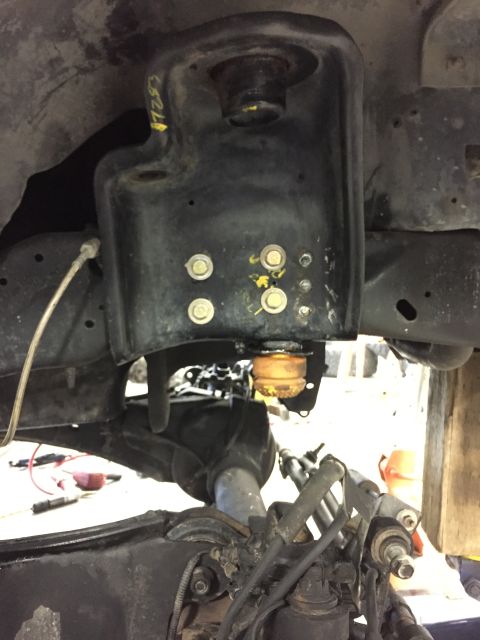 1984 Ford Bronco - Underside view of a vehicle's suspension system, showing a black metal component with yellow paint markings.