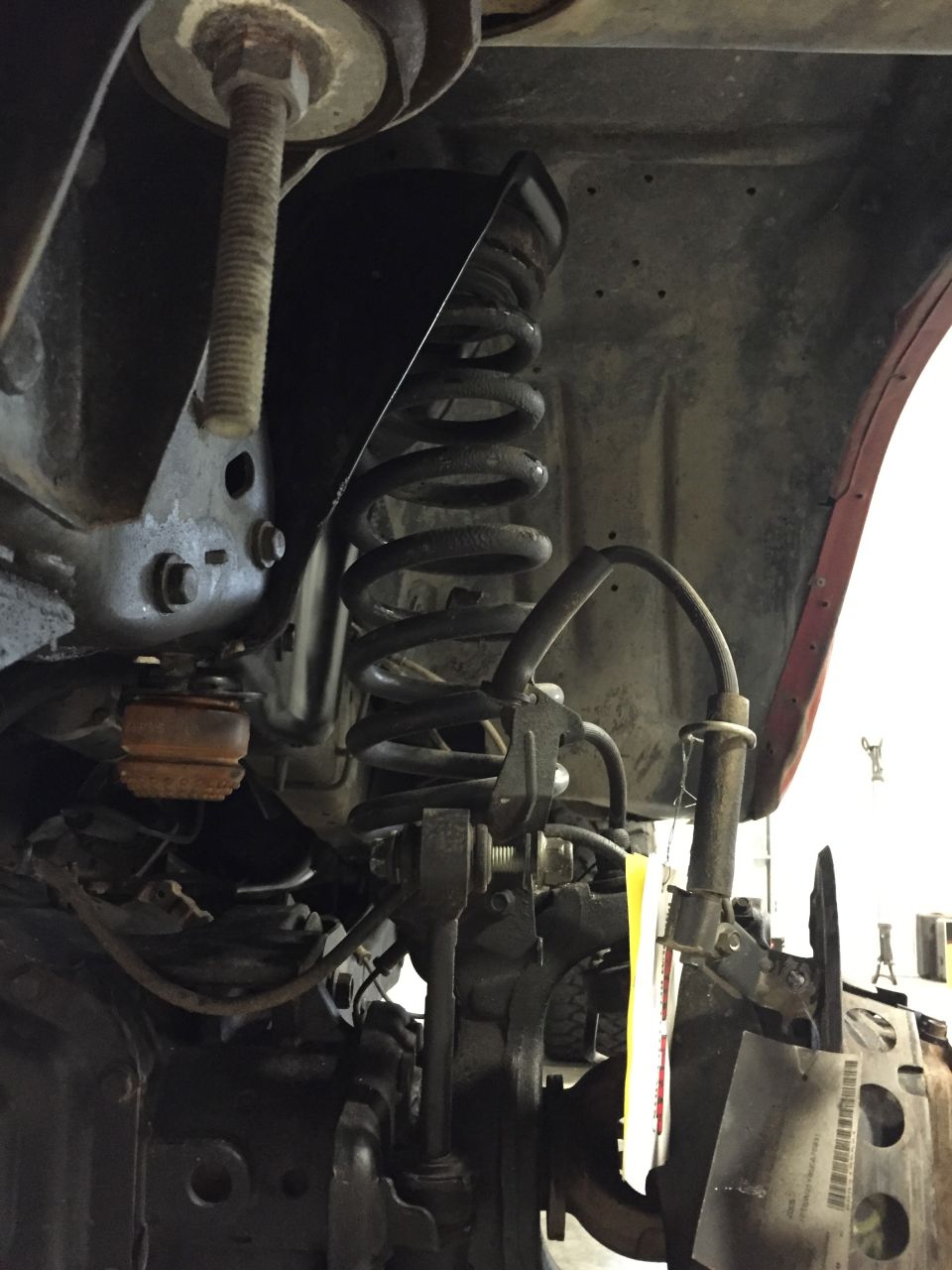 Underside view of red vehicle's front suspension with coil spring and brake line