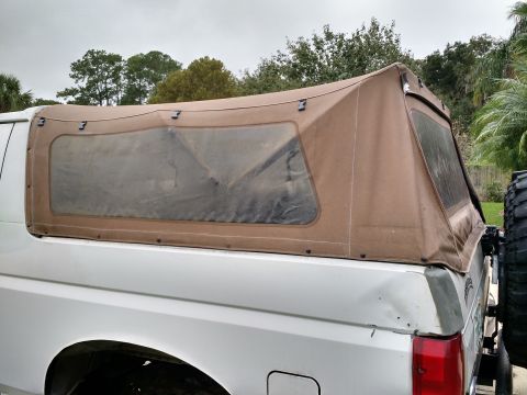 1992 Ford Bronco - The rear section of a white Ford Bronco features a tan soft top with clear plastic windows and a spare tire carrier.