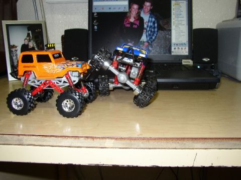 1989 Ford Bronco - Two RC monster trucks are positioned on a desk, with a laptop in the background showing a picture of two people.
