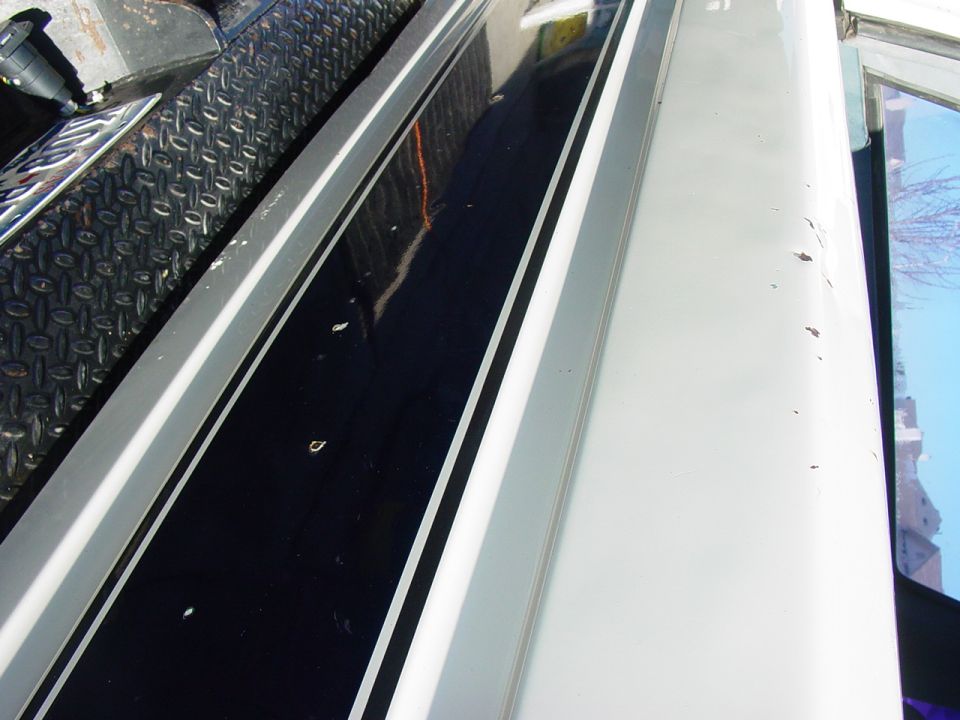 Close-up of white body panel with paint chips beside dark tinted window and chrome trim
