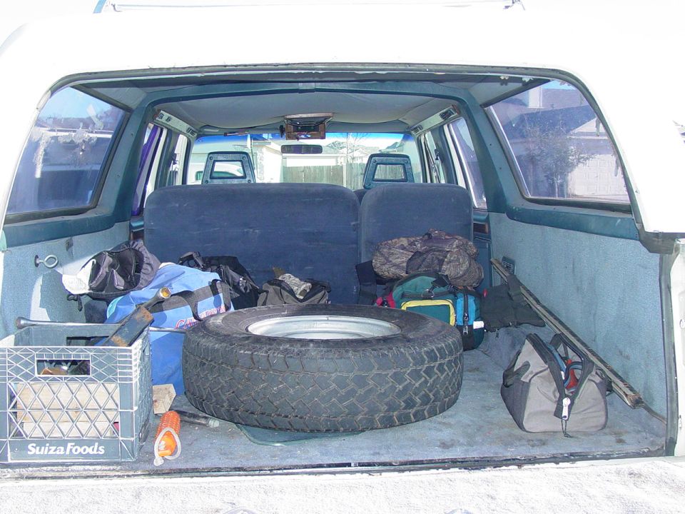 Rear cargo area of an SUV with a spare tire, duffel bags and a milk crate