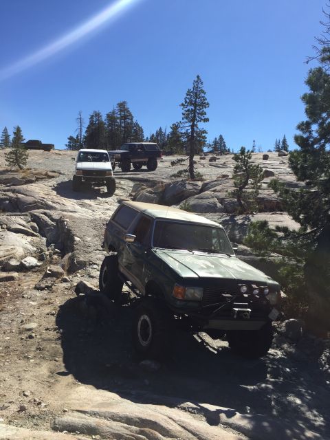 1989 Ford Bronco - Several off-road vehicles navigate a rocky trail under a clear blue sky.
