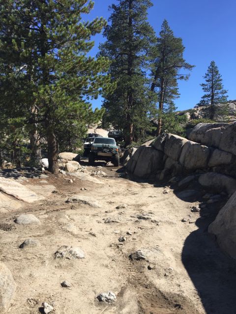 1989 Ford Bronco - A convoy of SUVs navigates a , off-road path through a rocky, wooded landscape under a clear blue sky.