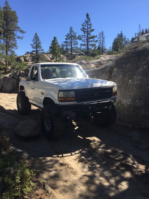 1989 Ford Bronco - Modified Ford F-150 navigates a rocky, off-road trail under a clear blue sky.