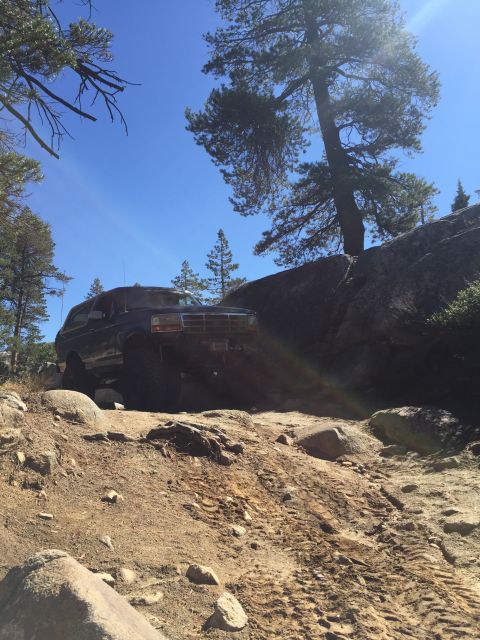 1989 Ford Bronco - A 1989 Ford Bronco tackles a challenging off-road path under a clear blue sky.