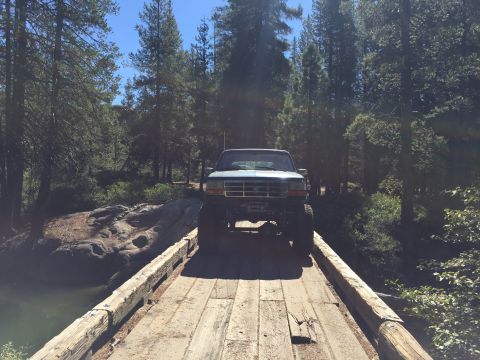 1989 Ford Bronco - Pickup truck crosses a rustic wooden bridge surrounded by trees.
