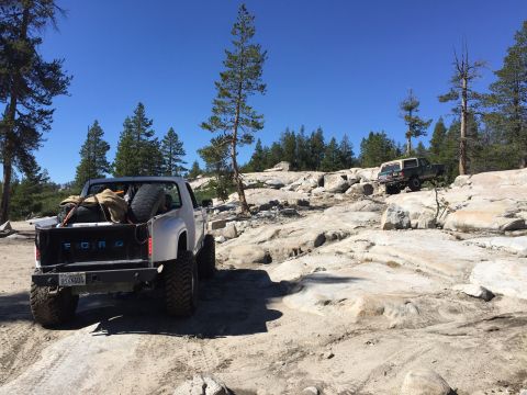 1989 Ford Bronco - Two off-road vehicles navigate a challenging rocky trail under a clear blue sky.