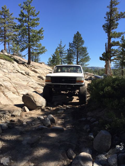 1989 Ford Bronco - A white pickup truck is shown off-roading on a sunny day with a clear blue sky overhead.