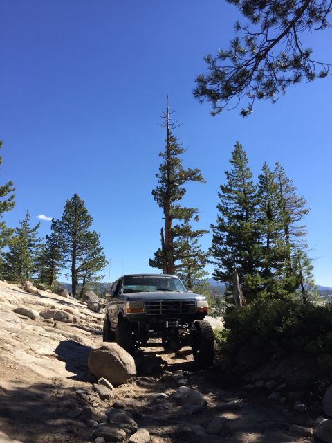 1989 Ford Bronco - 1989 Ford Bronco navigating a challenging off-road trail in a mountainous, wooded area.