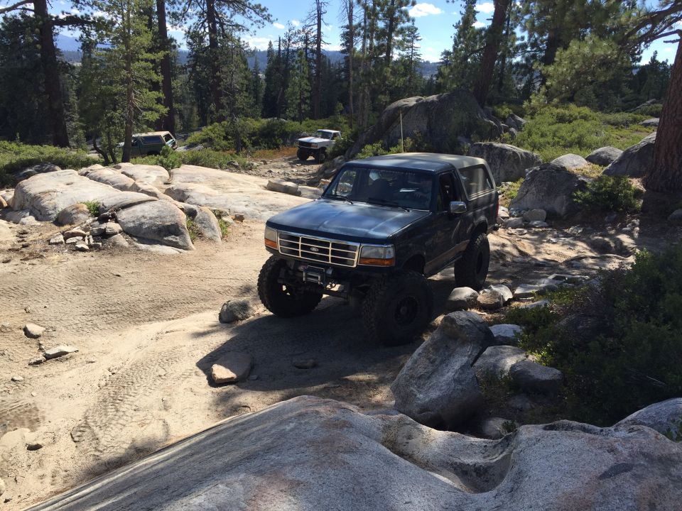 Dark blue Ford Bronco on rocky trail, other SUVs in background