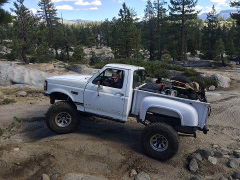 1989 Ford Bronco - This white pickup truck is equipped for off-road adventure, navigating a rocky terrain under a clear sky.