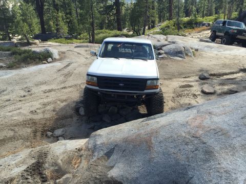 1989 Ford Bronco - White Ford F-150 truck navigating a rocky trail, with another off-road vehicle in the background.