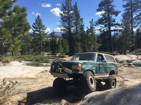 1989 Ford Bronco - This modified 1987 Ford Bronco navigates a challenging off-road course amidst a scenic, wooded landscape.