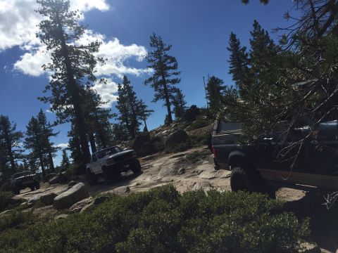 1989 Ford Bronco - Several off-road vehicles navigate a , rocky path under a bright blue sky with scattered clouds.