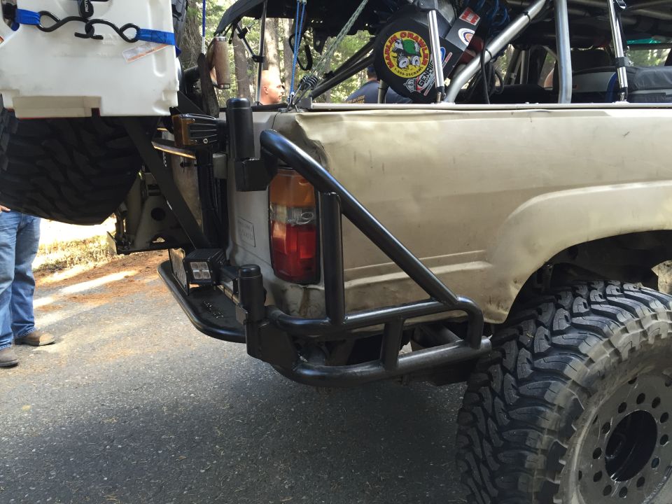 Rear view of a tan 1989 Ford Bronco with off-road modifications including a roll cage and spare tire carrier