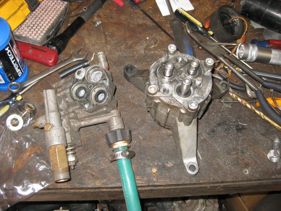 Two disassembled pressure washer pump components on a workbench with tools
