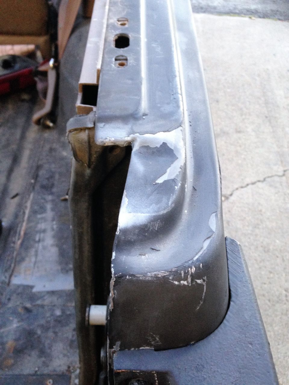 Close-up of a dented and scraped metal edge of a vehicle door, showing primer and chipped paint