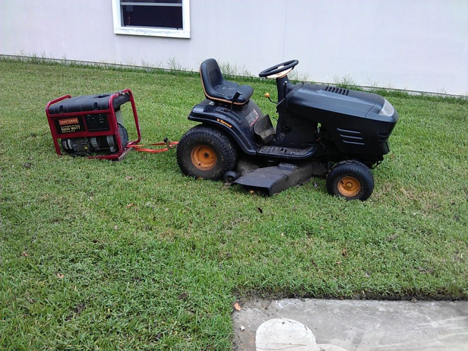 Black riding mower towing a red generator. No year visible