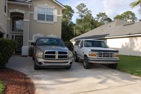 1994 Ford Bronco - A silver Dodge Ram and a white Ford Bronco are parked in a driveway in front of a house.