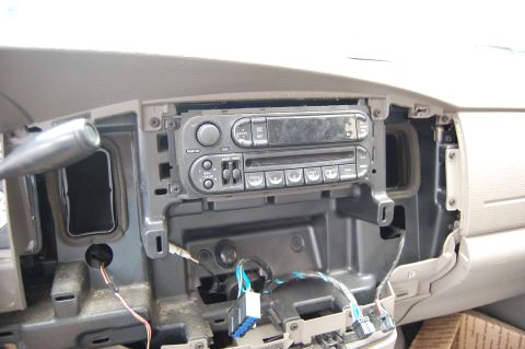 1994 Ford Bronco - The interior of a vehicle dashboard with the car stereo removed, revealing wiring and the cavity behind it. A portion of the gear shifter i…
