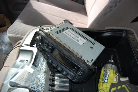 1994 Ford Bronco - A car stereo is partially removed and resting on the center console of a vehicle, with a bag of screws and a power drill nearby. The interi…