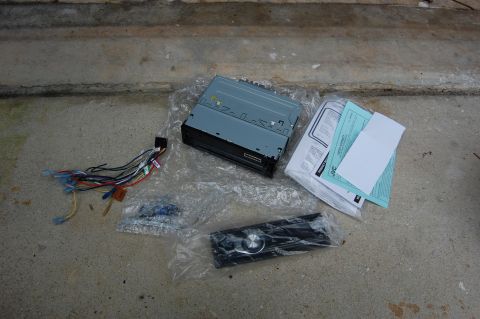 1994 Ford Bronco - The image shows car audio equipment laid out on a concrete surface. This includes a car stereo head unit, wiring harness, a detachable face…