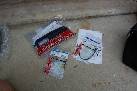 1994 Ford Bronco - A car stereo installation kit and wiring harnesses are laid out on a concrete surface. The kit includes a black dash trim piece and several…