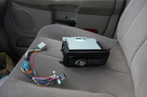 1994 Ford Bronco - A car stereo and wiring harness are laid out on the textured fabric of a car seat, with the car's door panel visible in the background.