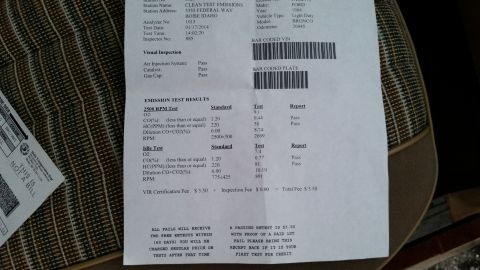 1981 Ford Bronco - A close-up of an emissions test results document with a vehicle's VIN and test results visible. The document is lying on a patterned fabric…