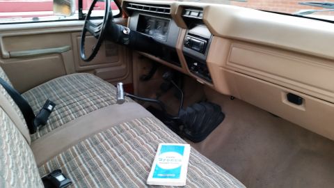 1981 Ford Bronco - The interior of a 1981 Ford Bronco is shown, featuring plaid fabric seats, a manual transmission shifter, and an owner's manual on the pass…