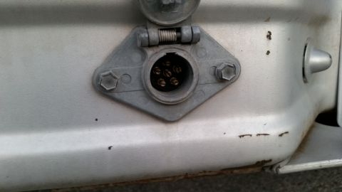 1981 Ford Bronco - A close-up view of a 7-pin trailer connector mounted on a silver vehicle. The connector has a hinged cover and is secured by two bolts.