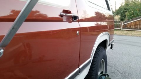 1981 Ford Bronco - Close-up side view of a vintage SUV's driver's side door and fender. The vehicle is a two-tone brown and white, with chrome accents on the…