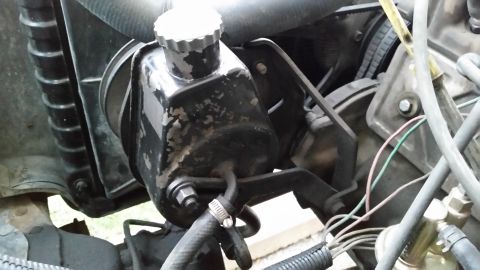 1981 Ford Bronco - A close-up view of a black power steering fluid reservoir with a silver cap, mounted in an engine bay. The reservoir shows signs of wear wi…