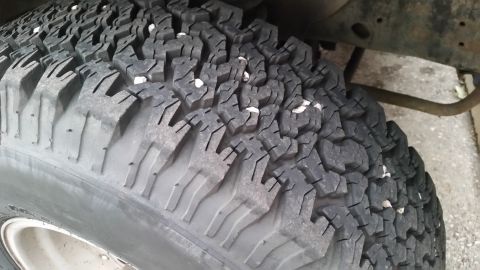 1981 Ford Bronco - A close-up view of a worn off-road tire with small white stones embedded in the tread. The tire is mounted on a vehicle with a rusty frame…