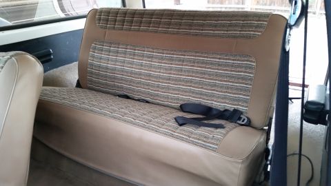 1981 Ford Bronco - The interior of a vintage Ford Bronco shows a rear bench seat with a brown and striped fabric pattern. Seat belts are visible across the se…