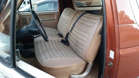 1981 Ford Bronco - Interior view of the driver's side of a vintage Ford Bronco, showing the patterned fabric front seats, steering wheel, and door panel. The…